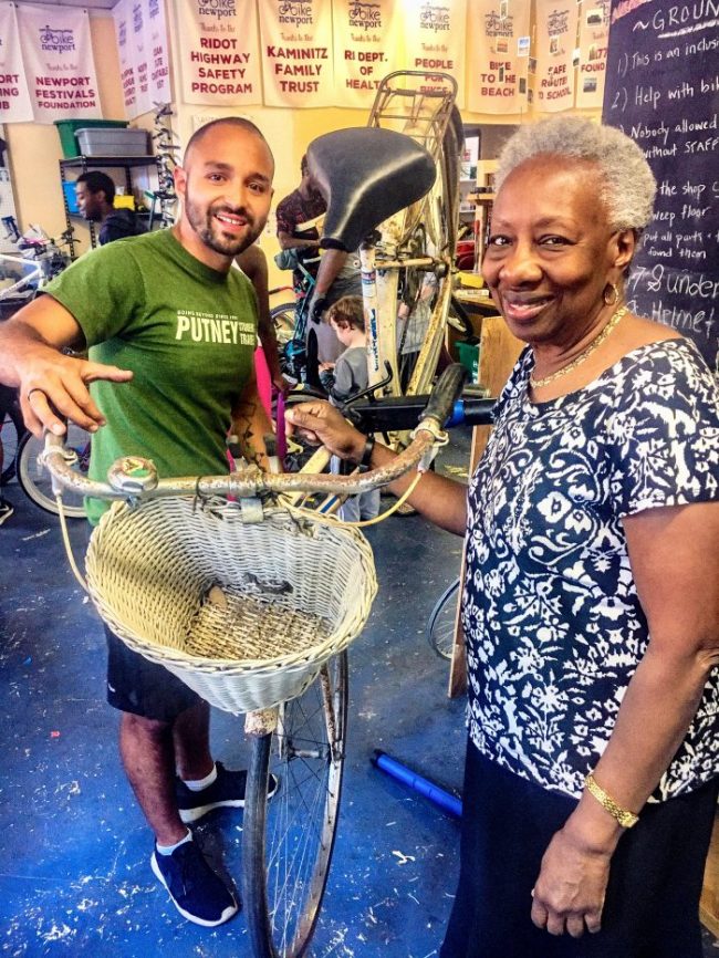 A young man helping an older woman repair her bicycle with a basket