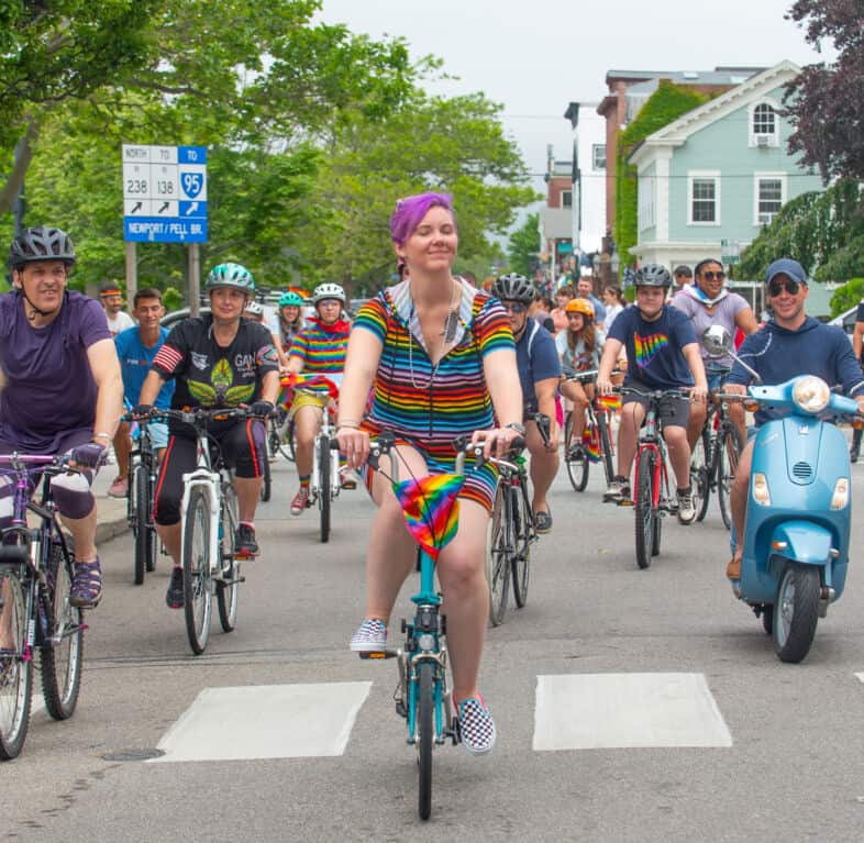 A smiling rider with pink hair leads the pack 