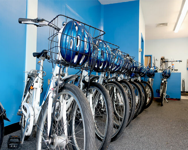 several bicycles with helmets in their baskets lined up for rental