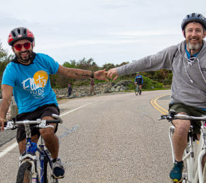 Two smiling men riding bikes and clasping hands