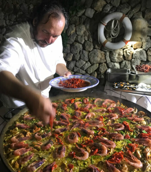 Man preparing large paella in a stone walled kitchen