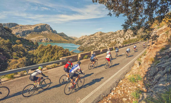 a group of cyclists riding on the road with Mallorcan mountains in the background