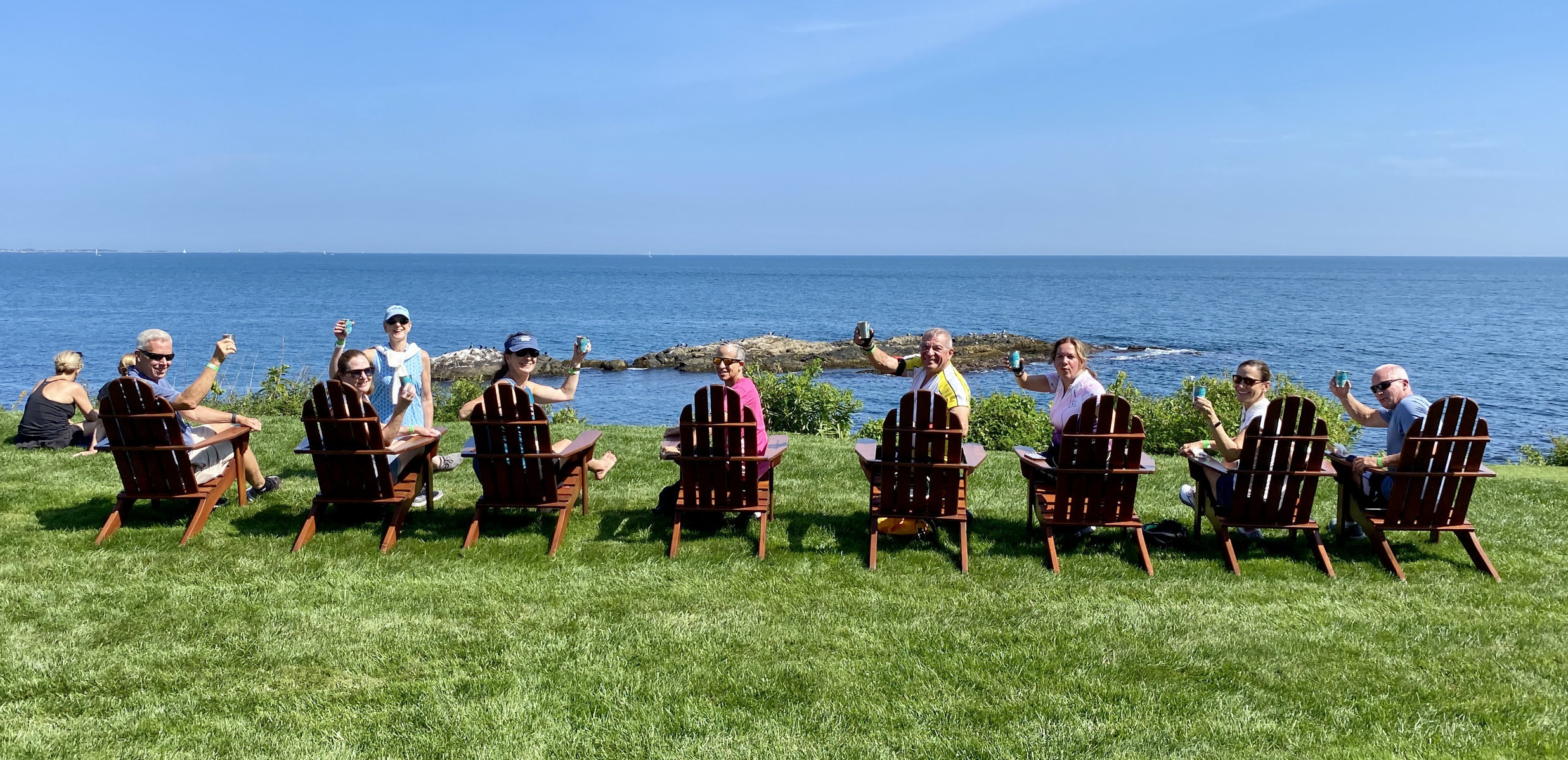 A group in lounge chairs before the sea looking back and raising their glasses