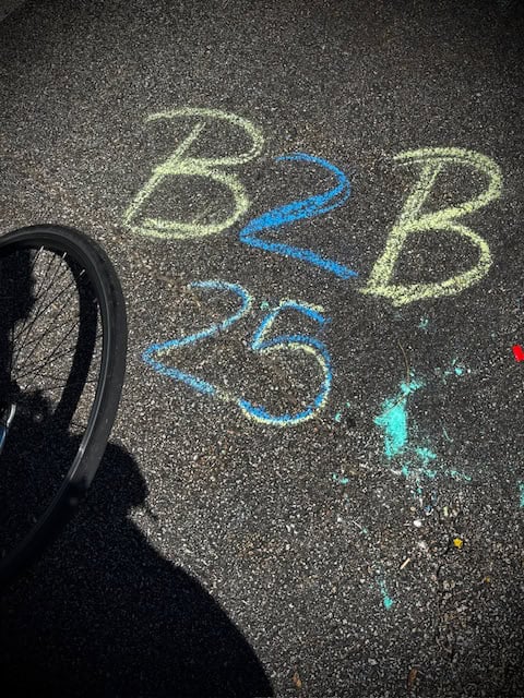 Vibrant street chalk art with B2B and 25 written on asphalt, part of Bike Newport community events and cycling celebrations.