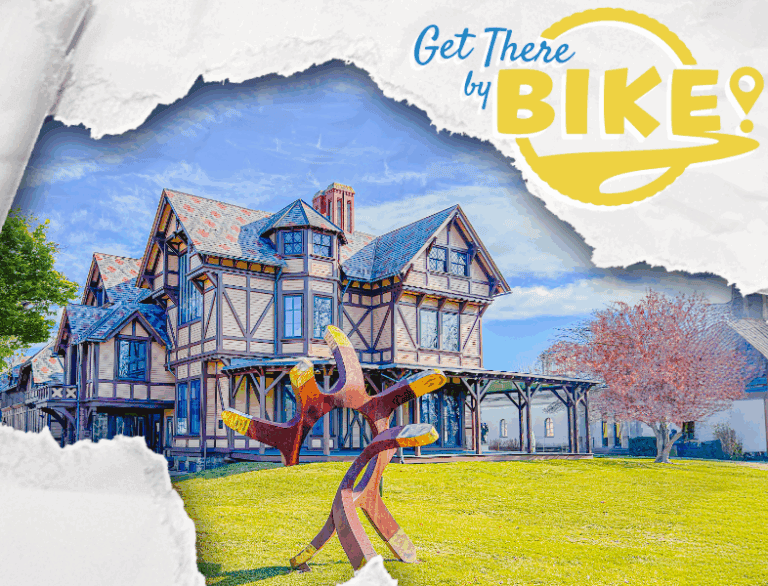 Colorful Victorian-style house with a large wooden bike sculpture in the front yard, sunny day, lush green grass, and pink flowering tree.