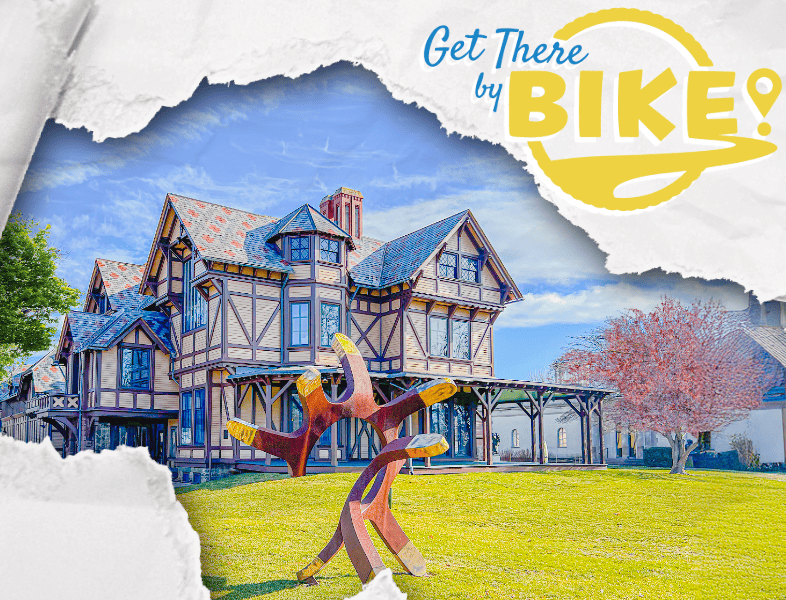 Colorful Victorian-style house with a large wooden bike sculpture in the front yard, sunny day, lush green grass, and pink flowering tree.