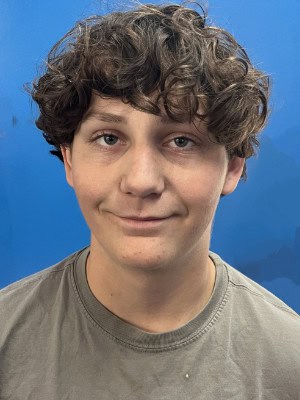 Young man with curly hair smiling, outdoor biking enthusiast wearing casual clothing at Bike Newport event, promoting sustainable transportation and cycling awareness.