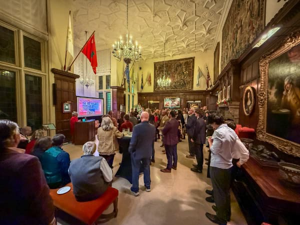 Historic downtown Newport, Rhode Island community event with people gathering in a grand, ornate room with flags and artwork, promoting biking and outdoor activities in Newport.