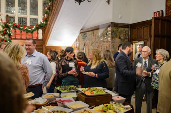 People at a bike-themed community event enjoying food and drinks in a historic indoor setting with holiday decorations for Bike Newport.