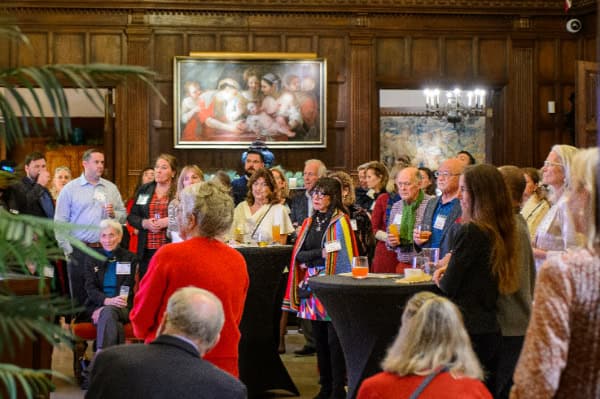 A diverse group of people attending a networking event at Bike Newport in a historic wood-paneled room with artwork on the wall.