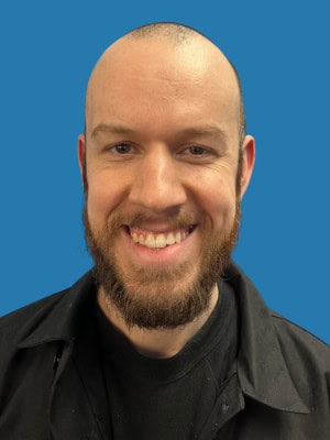Smiling man with beard and bald head, wearing black jacket against blue background, representing Bike Newport community and cycling initiatives.