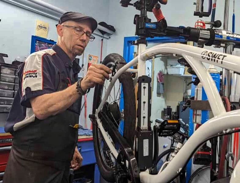 Professional bicycle mechanic repairing an e-bike at Bike Newport workshop, specializing in bike repairs and maintenance in Newport RI, promoting cycling safety and local biking community.