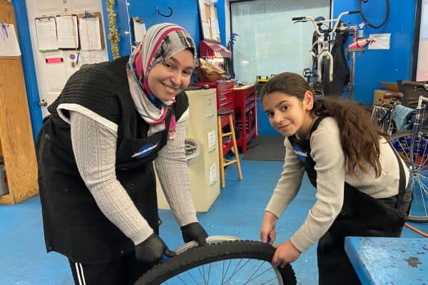 Diverse group of women and children repairing a bicycle at a community bike workshop emphasizing inclusion and cycling advocacy in Newport.