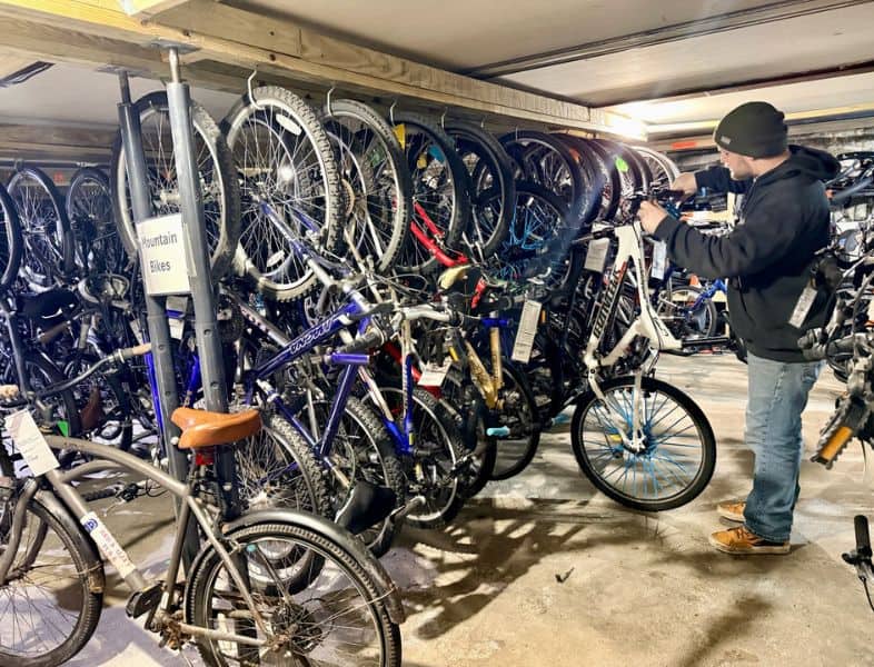 A person inspecting a variety of used bicycles stored in an indoor bike shop, emphasizing community reuse and sustainability.