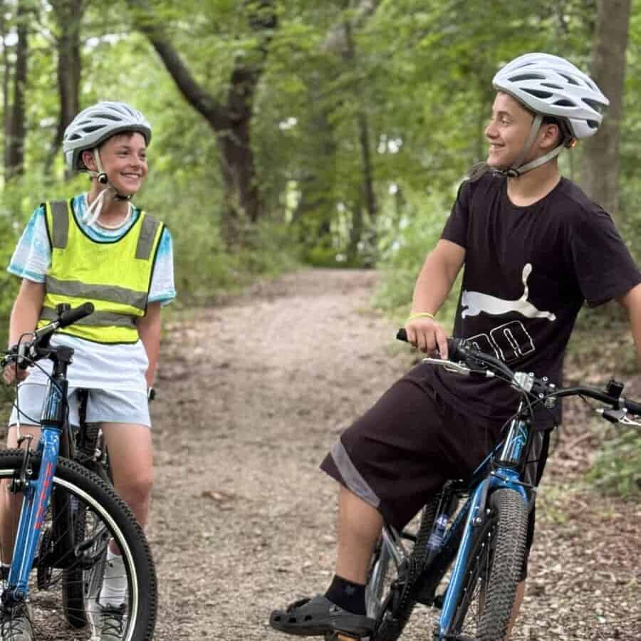 Two kids riding bikes with helmets in a lush green park, promoting diversity and inclusion in cycling advocacy.