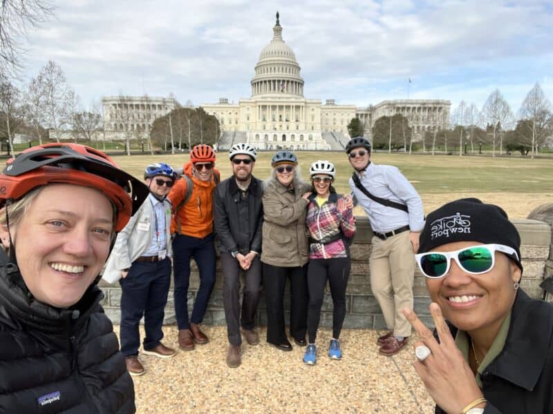 Diverse cycling advocates posing in front of the U.S. Capitol building during the National Bike Summit 2026, emphasizing inclusion and advocacy for all cyclists.