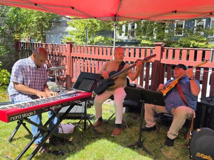 A four-piece string band with guitar, upright bass, mandolin and banjo performs under a white tent on a lawn.