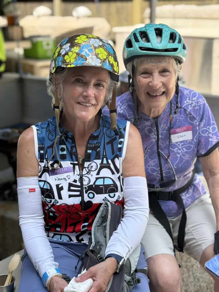 Two riders in helmets and name tags sit together and smile during a stop at the 10-Spot Ride.