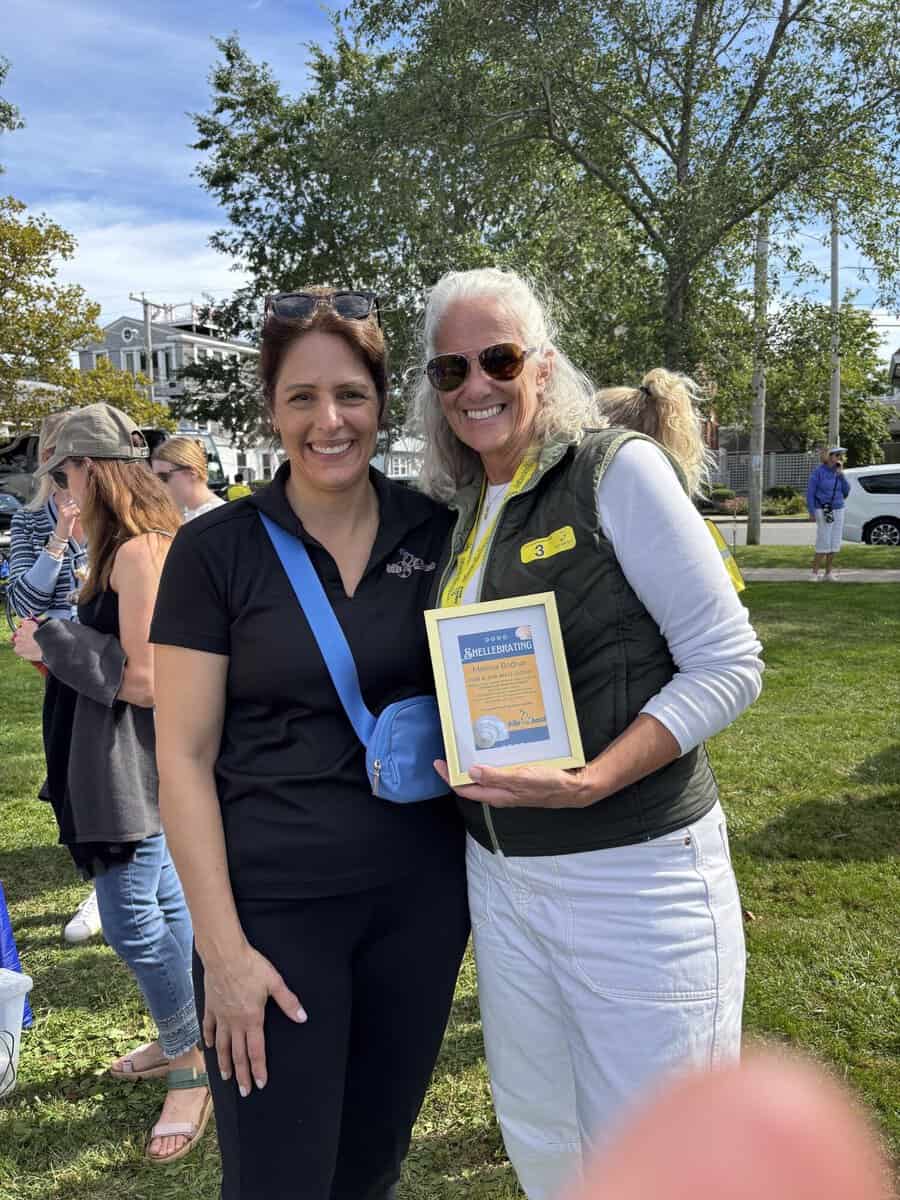 Two women smiling, one holding a framed 'Shellebrating Melissa Bodnar for a job well done' certificate